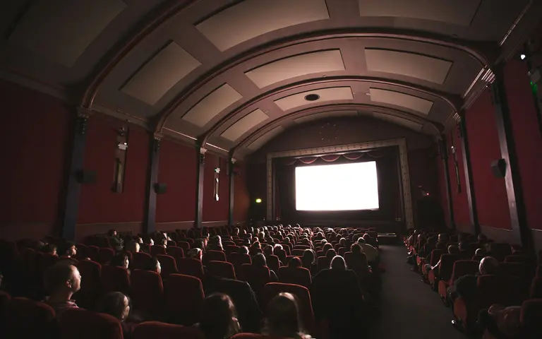 Publika u zamračenoj sali gleda ka osvetljenom platnu