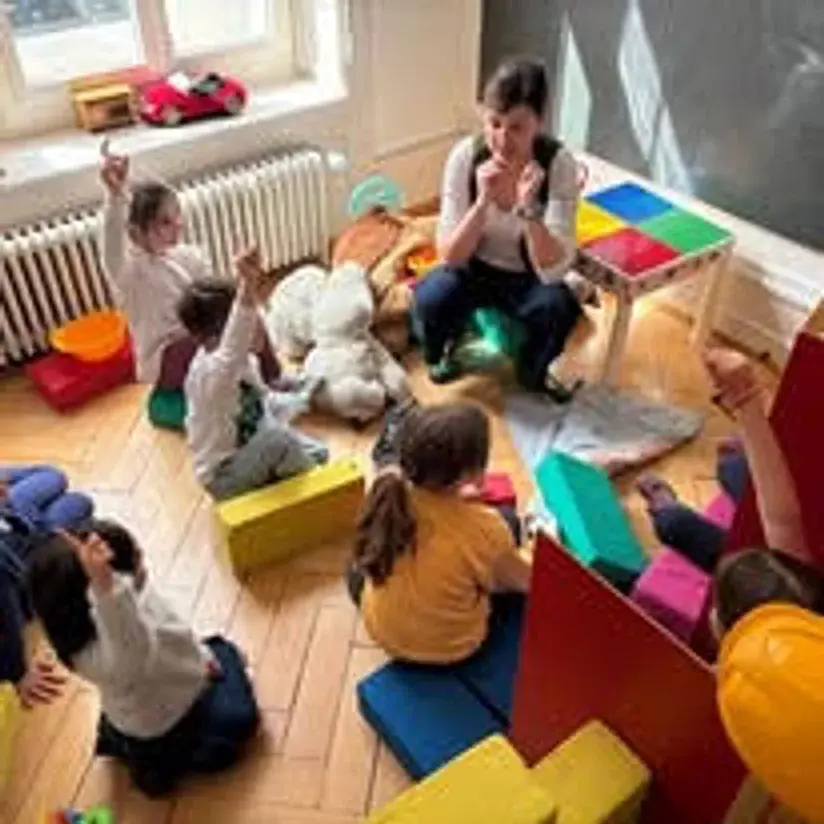 Vaspitačica sedi na podu igraonice okružena decom koja se igraju
