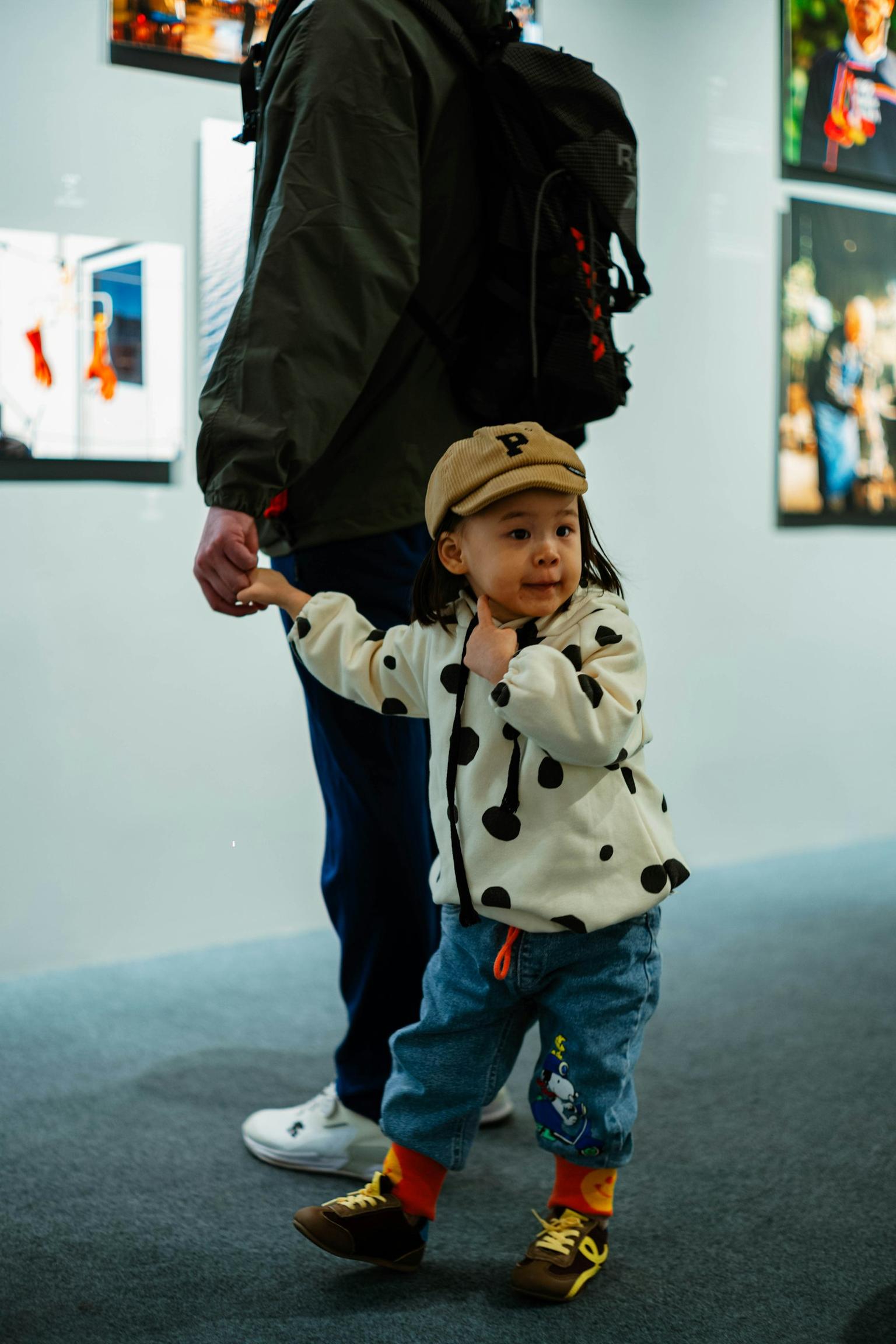 A child in a cap holding an adult's hand while looking around a photography exhibition